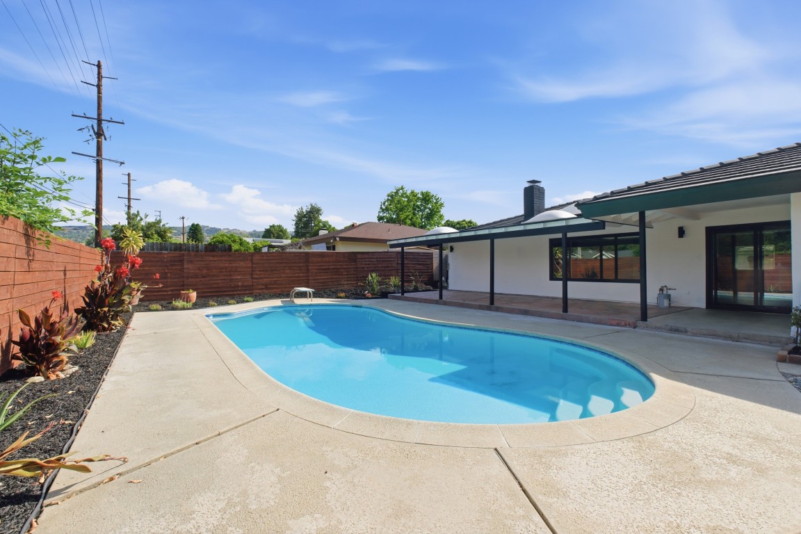 Backyard after renovation — restored pool, horizontal-slat privacy fence, fresh landscaping under a clear sky