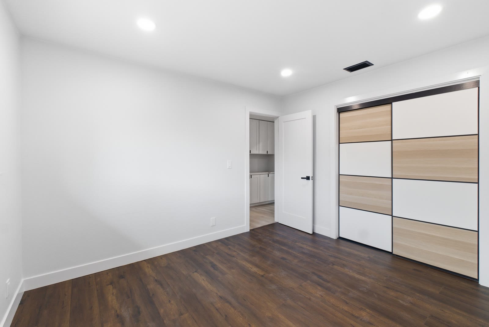 Secondary bedroom — two-tone sliding closet doors, dark wide-plank flooring