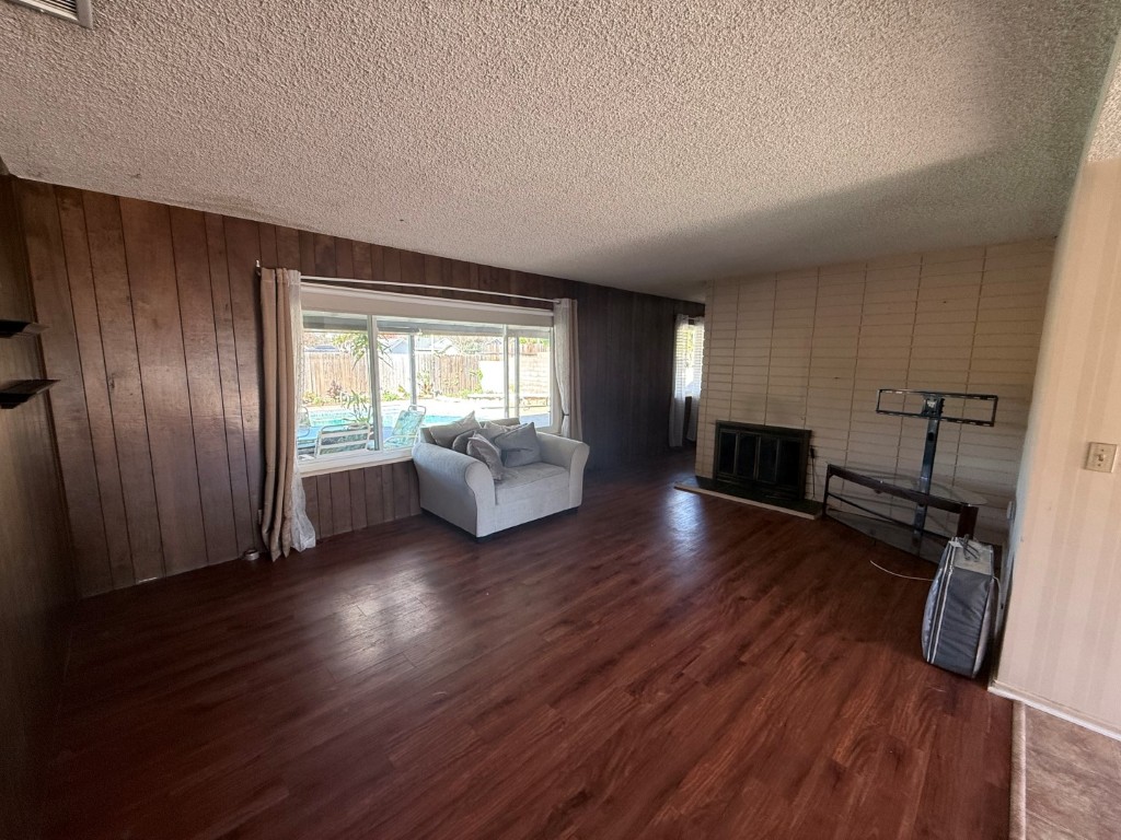 Living room before renovation — dark wood-paneled walls, popcorn ceiling, dated flooring