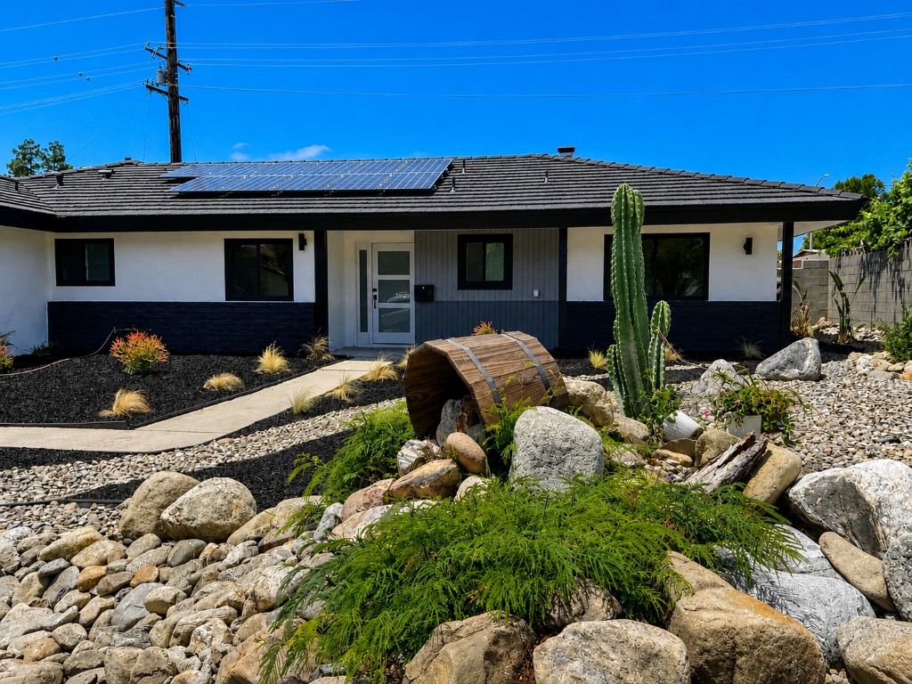 Front exterior after renovation — black-trim facade, fresh paint, dryscape yard with barrel water feature