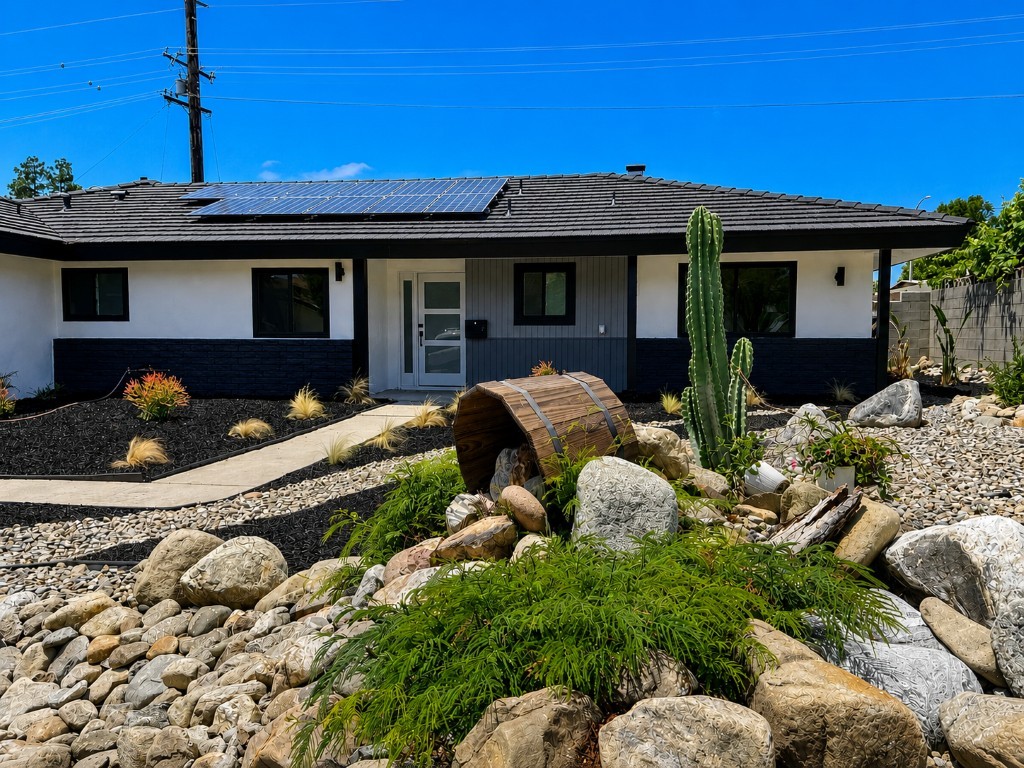 Front exterior in daylight — black trim, rooftop solar, dryscape yard with cactus and barrel water feature