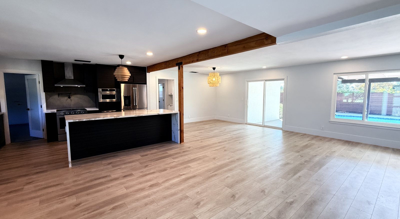 Great room from the entry side: kitchen island and wood beam at left, sliding door and wide window looking out to the pool