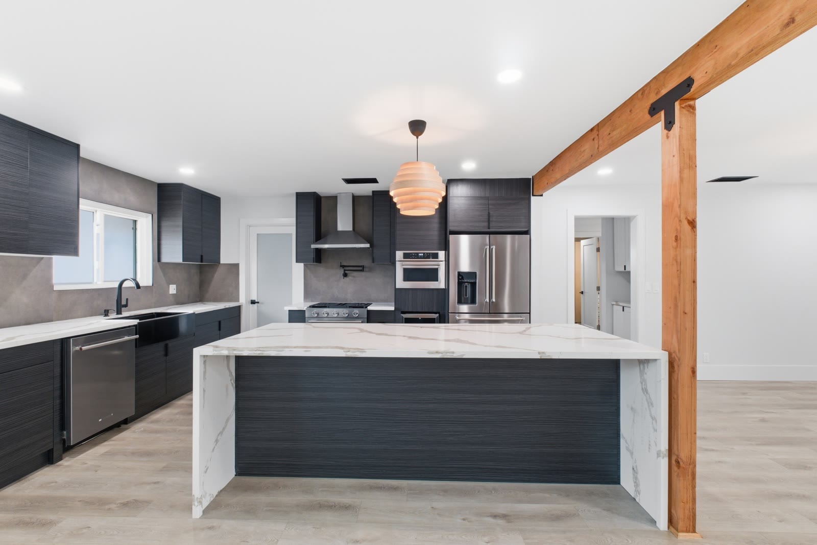Kitchen head-on — waterfall quartz island, dark Euro-style cabinetry, range wall with pot filler, wood beam accent