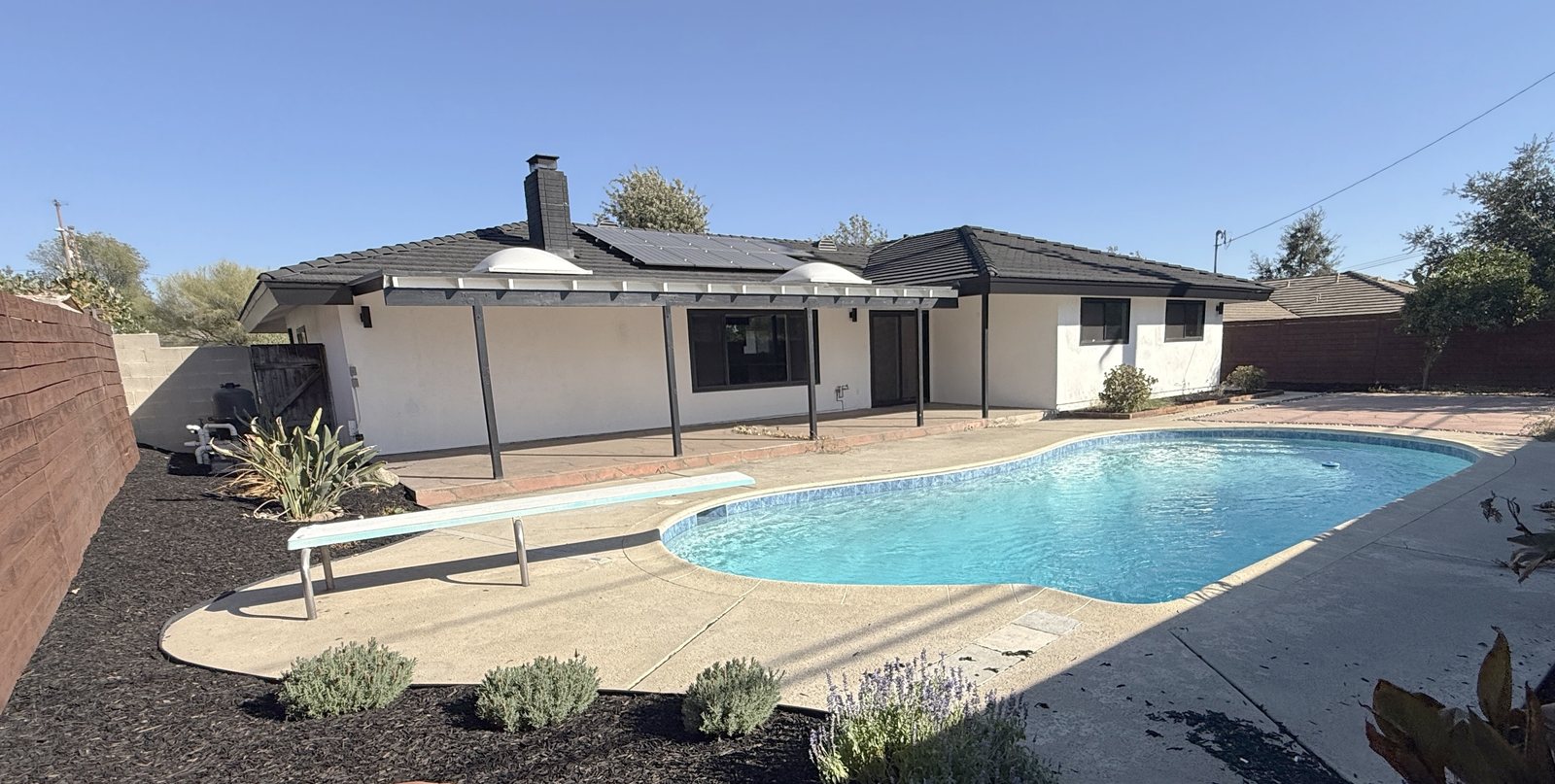 Rear of the home in daylight, with the restored pool, covered patio, and rooftop solar panels