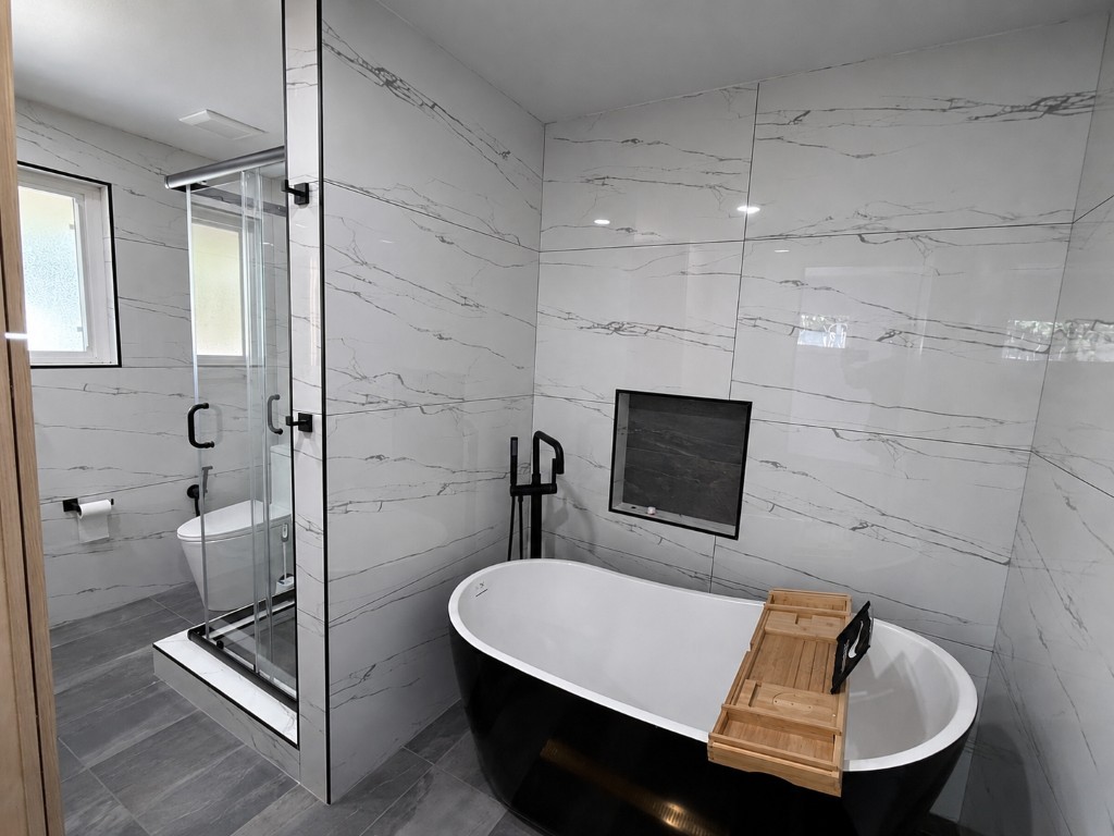 Primary bath — freestanding black slipper tub, matte-black floor-mount filler, floor-to-ceiling marble-look tile, glass shower