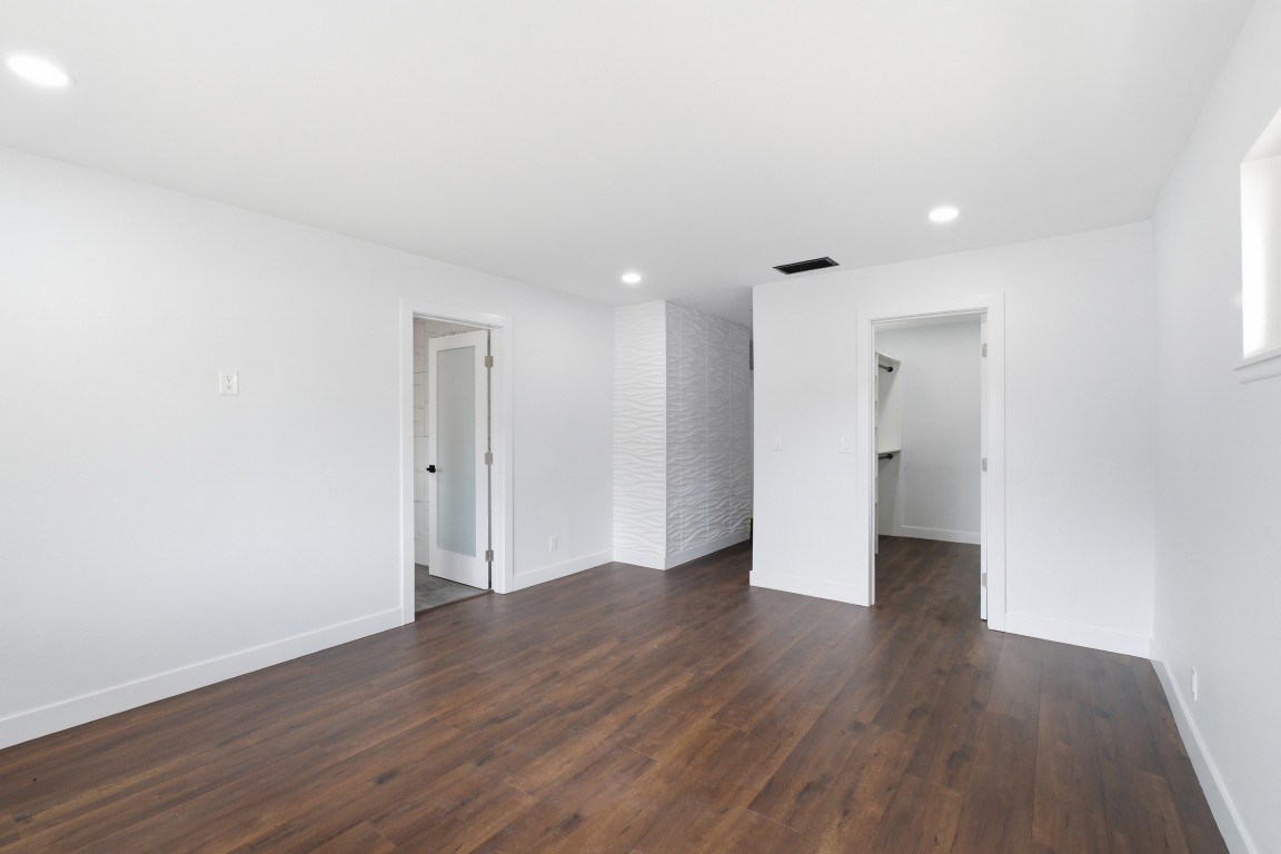 Primary bedroom with a 3D wave accent wall, doors to the ensuite and walk-in closet, dark wide-plank flooring